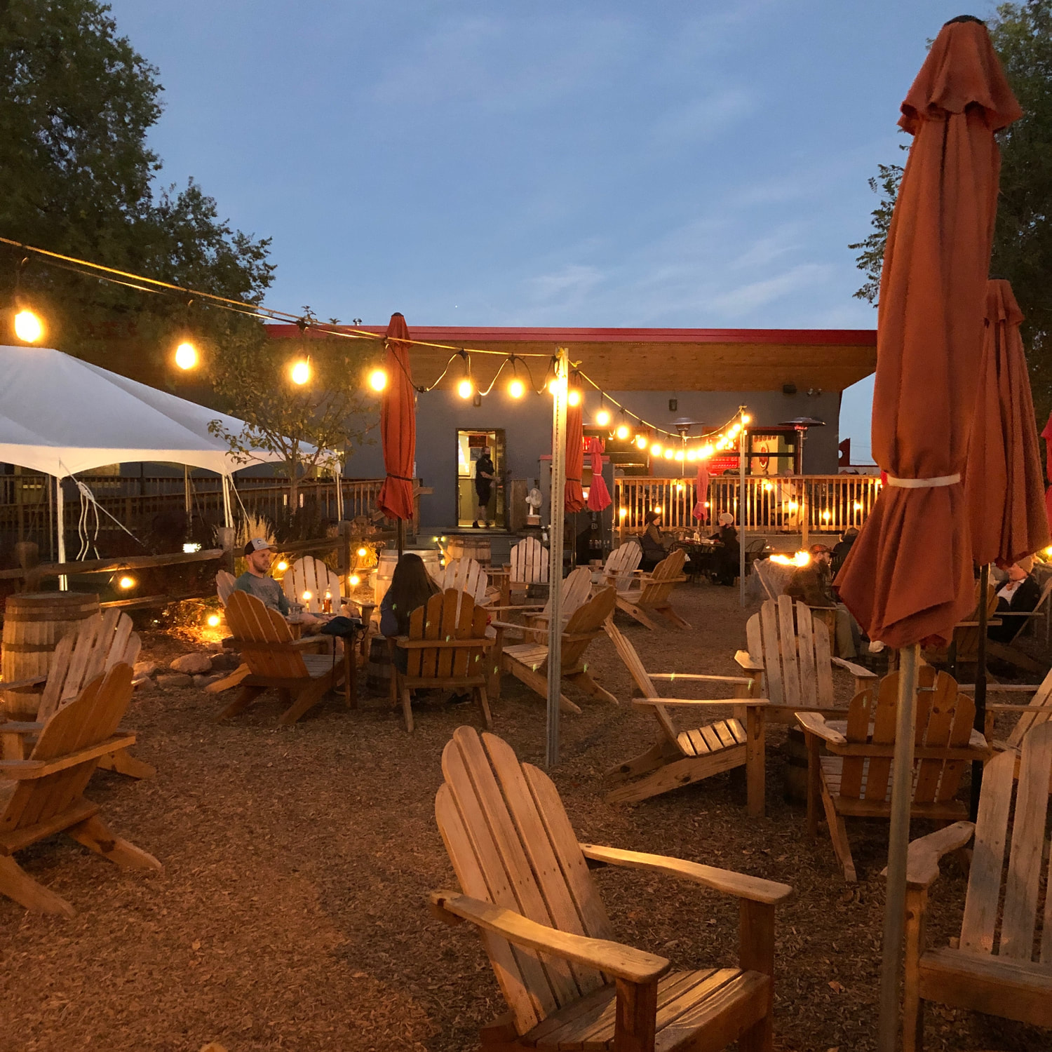 Outdoor beer garden patio in early evening, lit up by decorative lighting.