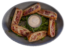A plate of Rueben rolls with dipping sauce and garnish.